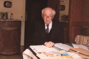 Zdjęcie przedstawiające prof. Zygmunta Ziembińskiego siedzącego przy stole pełnego książek i zapisków