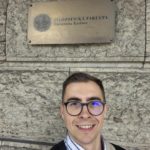 mgr M. Grabarczyk na tle znaku Uniwersytetu