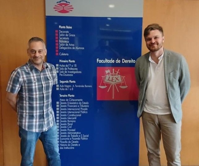 Zdjęcie dr. M. Krotoszyńskiego z prof. Xulio Ferreiro Baamonde na tle loga Wydział Prawa Uniwersytetu w A Coruña